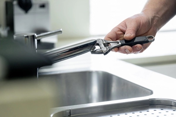 Adjustable wrench closed around the base of a black kitchen mixer tap